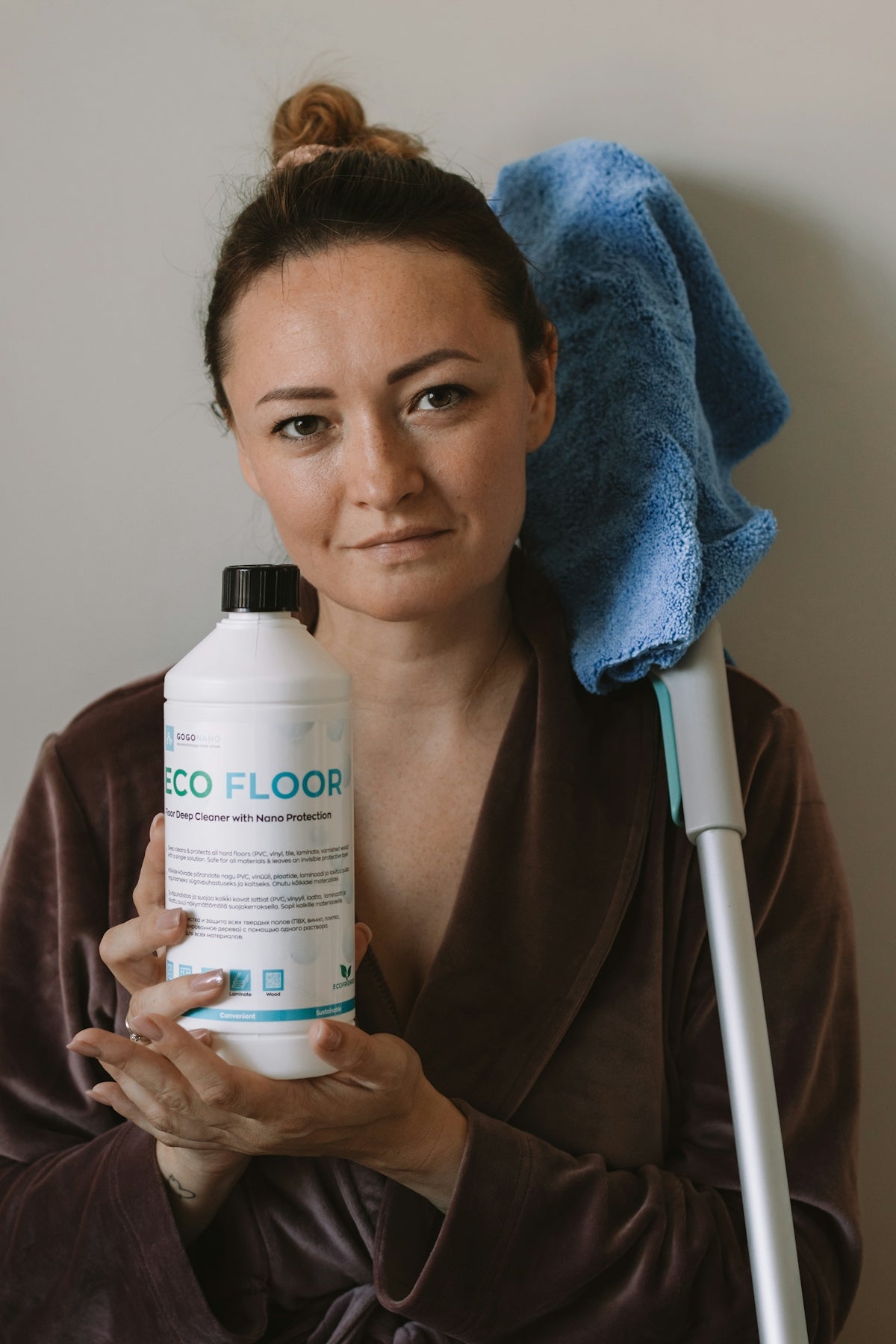 Woman holds floor cleaner and mop.